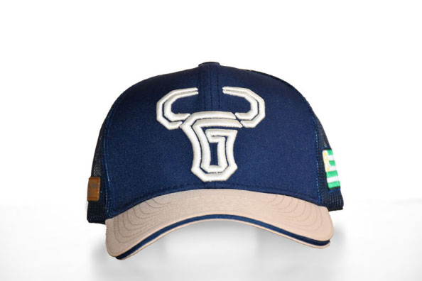 Gorra trucker azul marino con la visera beige y malla negra, mostrando un logo de toro estilizado en blanco bordado al frente. En el lateral tiene una bandera verde, blanca y amarilla.